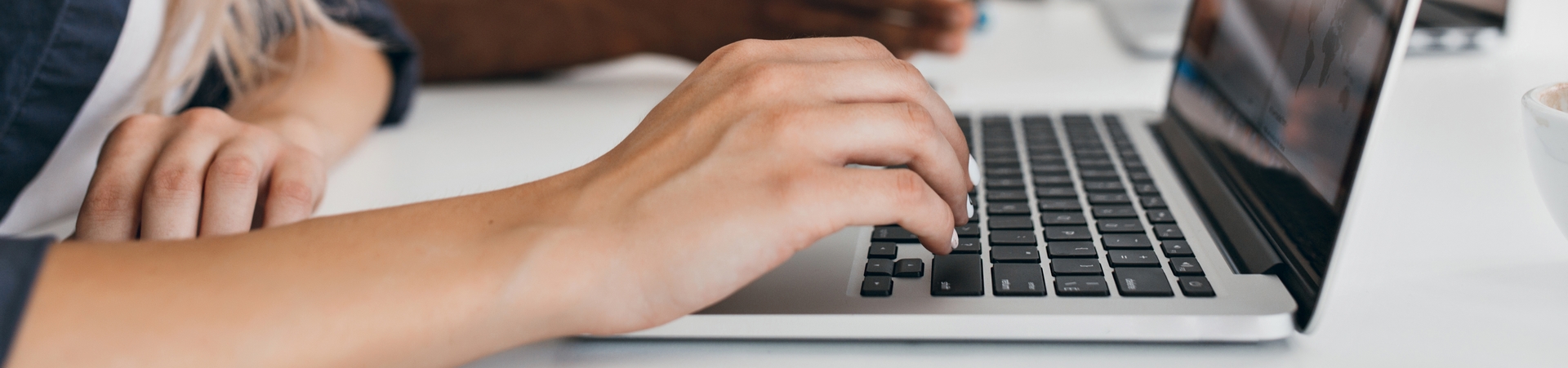 Blonde woman with elegant hairstyle typing text on keyboard in office. Indoor portrait of international employees with secretary using laptop on foreground..